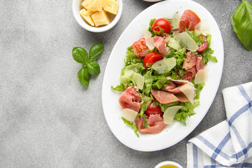 Salad with jamon (parma, ham, serrano, prosciutto), parmesan cheese, lettuce, cherry tomatoes on a plate. Delicious lunch, healthy food, Italian (spanish) cuisine