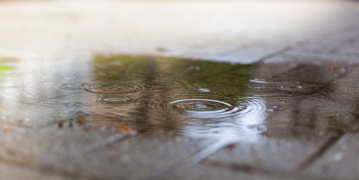 Puddle on street with raindrops. Wasserpfütze mit Regentropfen auf Straße.