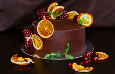 gorgeous chocolate cake decorated with slices of baked orange and fresh pomegranate with a sprig of mint on a dark brown background