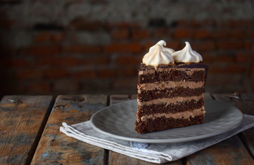 Piece of chocolate cake decorated with rosettes of meringue cream: chocolate-nut biscuit, caramel cream. Homemade baking.