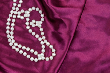 Pearl necklace on purple satin fabric background