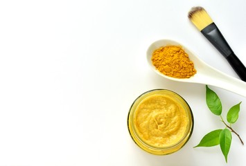 Turmeric powder and homemade facial mask for acne skin in small glass jar, top view, copy space.