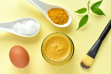 Facial mask for wrinkles with turmeric powder, coconut oil and egg white, flat lay on yellow background.