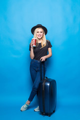 Obraz na płótnie Canvas Beautiful young woman smiling and pulling colour luggage isolated on blue background. Blonde woman going to summer vacation. Travel trip funny.