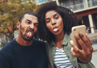 Young couple making funny face while taking selfie on smart phone