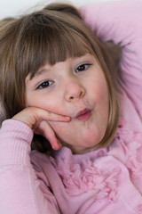 Vertical closeup portrait of pretty little girl in pink sweater lying down making a funny pouty face