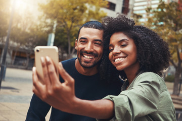 Smiling young couple taking selfie in city park
