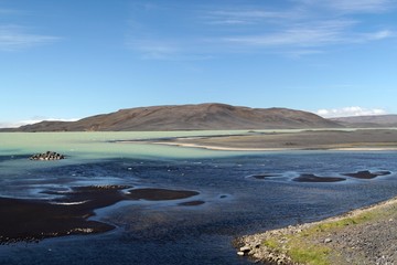 Black and green contrasting water at remote Hálslón lake in Iceland with small black sand banks