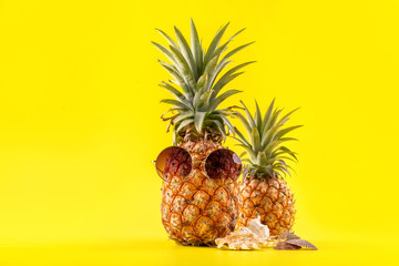 Creative pineapple looking up with sunglasses and shell isolated on yellow background, summer vacation beach idea design pattern, copy space close up