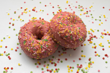 one pink donuts on another with sprinkles with a white background