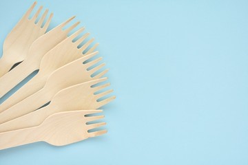 Wooden disposable forks on blue background, natural eco friendly, zero waste product, top view with copy space.