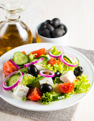 Fresh Greek salad made of cherry tomato, ruccola, arugula, feta, olives, cucumbers, onion and spices. Caesar salad in a white bowl on wooden background. Healthy organic diet food concept.
