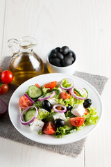Fresh Greek salad made of cherry tomato, ruccola, arugula, feta, olives, cucumbers, onion and spices. Caesar salad in a white bowl on wooden background. Healthy organic diet food concept.