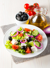 Fresh Greek salad made of cherry tomato, ruccola, arugula, feta, olives, cucumbers, onion and spices. Caesar salad in a white bowl on wooden background. Healthy organic diet food concept.