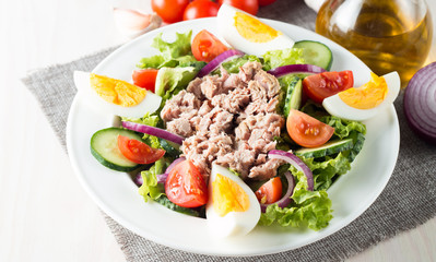 Fresh fish tuna salad made of tomato, ruccola, tuna, eggs, arugula, crackers and spices. Caesar salad in a white bowl on wooden background