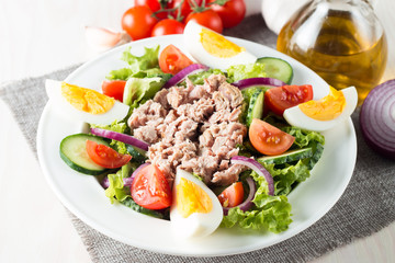 Fresh fish tuna salad made of tomato, ruccola, tuna, eggs, arugula, crackers and spices. Caesar salad in a white bowl on wooden background