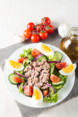 Fresh fish tuna salad made of tomato, ruccola, tuna, eggs, arugula, crackers and spices. Caesar salad in a white bowl on wooden background