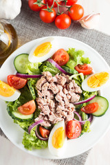 Fresh fish tuna salad made of tomato, ruccola, tuna, eggs, arugula, crackers and spices. Caesar salad in a white bowl on wooden background