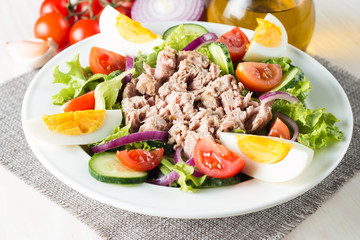 Fresh fish tuna salad made of tomato, ruccola, tuna, eggs, arugula, crackers and spices. Caesar salad in a white bowl on wooden background