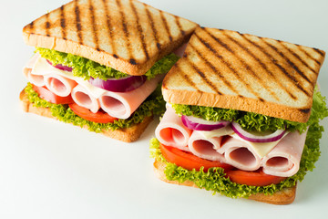 Close-up photo of a club sandwich. Sandwich with meat, prosciutto, salami, salad, vegetables, lettuce, tomato, onion and mustard on a fresh sliced rye bread on wooden background. Olives background.