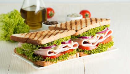 Close-up photo of a club sandwich. Sandwich with meat, prosciutto, salami, salad, vegetables, lettuce, tomato, onion and mustard on a fresh sliced rye bread on wooden background. Olives background.