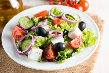 Fresh Greek salad made of cherry tomato, ruccola, arugula, feta, olives, cucumbers, onion and spices. Caesar salad in a white bowl on wooden background. Healthy organic diet food concept.