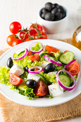 Fresh Greek salad made of cherry tomato, ruccola, arugula, feta, olives, cucumbers, onion and spices. Caesar salad in a white bowl on wooden background. Healthy organic diet food concept.