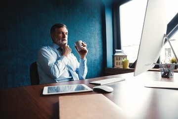Focused mature businessman deep in thought while sitting at a table in modern office.