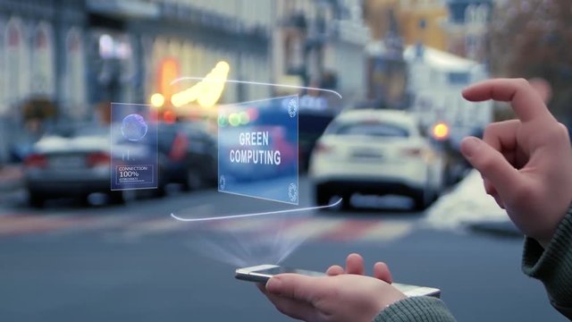 Female hands on the street interact with a HUD hologram with text Green computing. Woman uses the holographic technology of the future in the smartphone screen on the background of the evening city