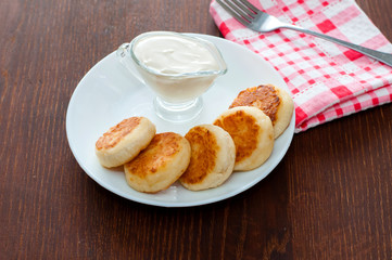 Cheese pancakes with sour cream on a white plate on a pink napkin with a fork