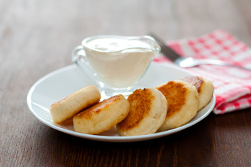 Cheese pancakes with sour cream on a white plate on a pink napkin with a fork, side view. Can be used for menu design.