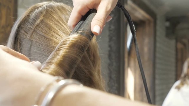 Hairdresser is straightening the client's hair in a beauty salon.