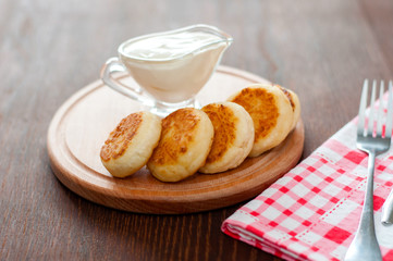 Cheese pancakes with sour cream on a wooden board, with a fork and napkin horizontal format.