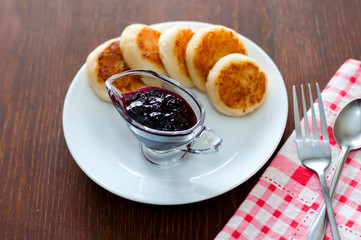 Cheese pancakes with currant jam, on a white plate with a fork, a teaspoon and a napkin, view from the top.