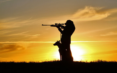Silhouette of a girl with a rifle at sunset with a dog, a breed of Belgian Shepherd Malinois dog