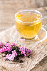 Cup of tea and pink spring cherry blossoming on wooden table with petals