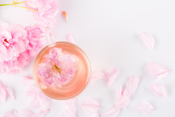 Obraz na płótnie Canvas Cup of pink cherry blossom herb tea on white, Top view