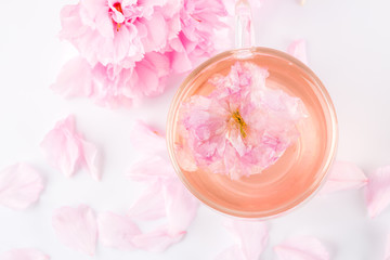 Cup of pink cherry blossom herb tea on white, Top view