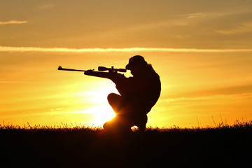Fototapeta na wymiar Silhouette of a man with a rifle on the background of a beautiful sunset, the boy shoots a gun