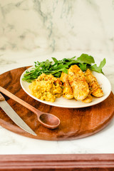 Crispy zucchini fries with garlic hummus sausea nd arugula on round wooden board. Copy space on a white marble background.