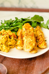 Crispy zucchini fries with garlic hummus sausea nd arugula on round wooden board. Copy space on a white marble background.Close-up.
