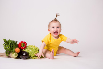 baby girl smiling in yellow bodysuit on white background with vegetables, baby food concept