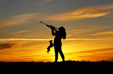 Fototapeta na wymiar Silhouette of a girl with a rifle at sunset with a dog, a breed miniature pinscher