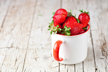 Organic red strawberries in white ceramic cup on rustic wooden background. Healthy sweet food, vitamins and fruity concept.