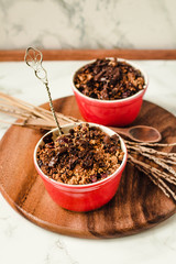 Granola crumble in two cups with malted chocolate on a wooden round board. Selective focus.