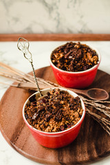 Granola crumble in two cups with malted chocolate on a wooden round board. Selective focus.