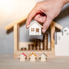 Fototapeta na wymiar Real estate or property investment growing business. Home mortgage loan rate. Saving money for retirement concept. Male hand holding house model with blurred coin stack in house frame on the table.