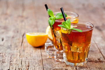 Traditional iced tea with lemon, mint leaves and ice cubes in two glasses on rustic wooden table background.
