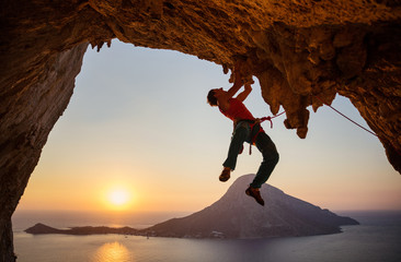 Male rock climber on challenging route on cliff at sunset