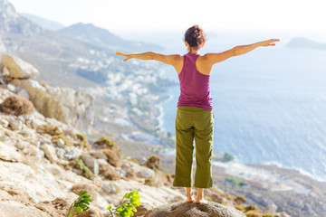 Young Caucasian woman practicing yoga while standing on cliff on sea coast